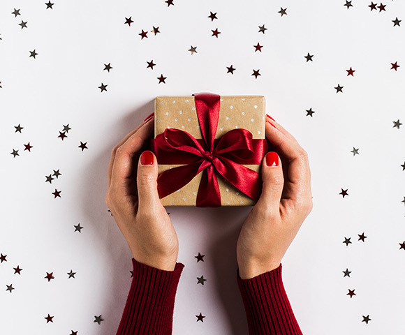 Mãos segurando caixa com laço de presente. Aproveite para comprar perfumes de presente de Natal com dicas do Blog Sieno